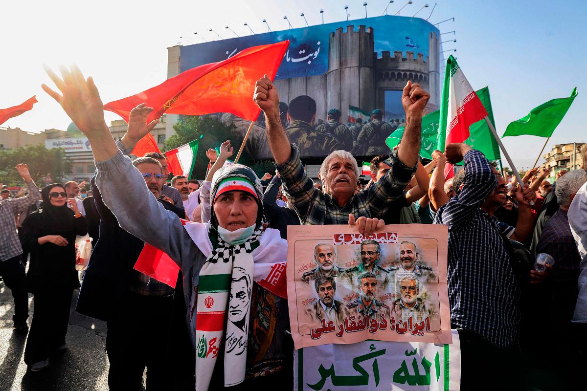Iranians lift flags and placards during a rally protesting the US attack on Iran in Enghelab Square in Tehran on June 22, 2025. Iran’s President Masoud Pezeshkian condemned US strikes on nuclear sites on June 22, saying in his first response that the attack revealed Washington was “behind” Israel’s military campaign in the Islamic republic. - ATTA KENARE / AFP
