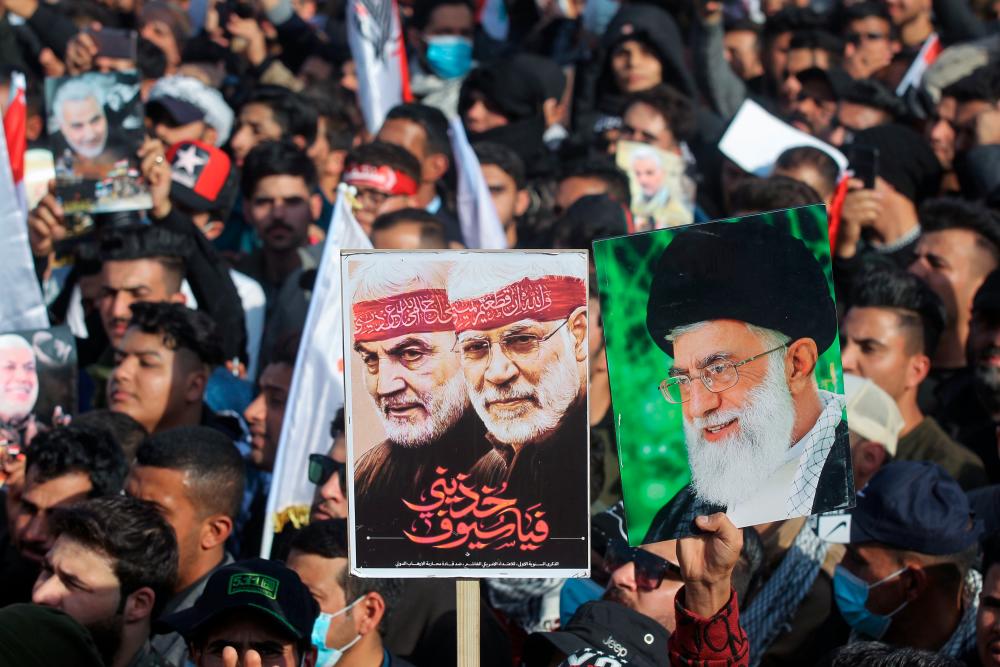 Iraqi demonstrators lift a placards depicting Iraqi commander Abu Mahdi al-Muhandis (C) and Iranian Revolutionary Guards commander Qasem Soleimani (L) and Iran’s Supreme Leader Ayatollah Ali Khamenei (R) during a rally marking one year since the killing of the two commanders in a US drone strike, in Tahrir square in the capital Baghdad on January 3, 2021. AFP / AHMAD AL-RUBAYE