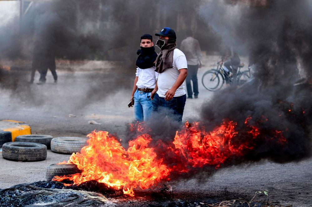 Masked Iraqi protesters stand next to burning tires at a roadblock in the central holy shrine city of Najaf on Nov 18. — AFP