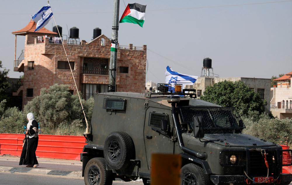 An Israeli military vehicle drives while displaying Israeli flags past a lamp post displaying a Palestinian flag in the town of Huwara near Nablus in the occupied West Bank on May 30, 2022. AFPPIX