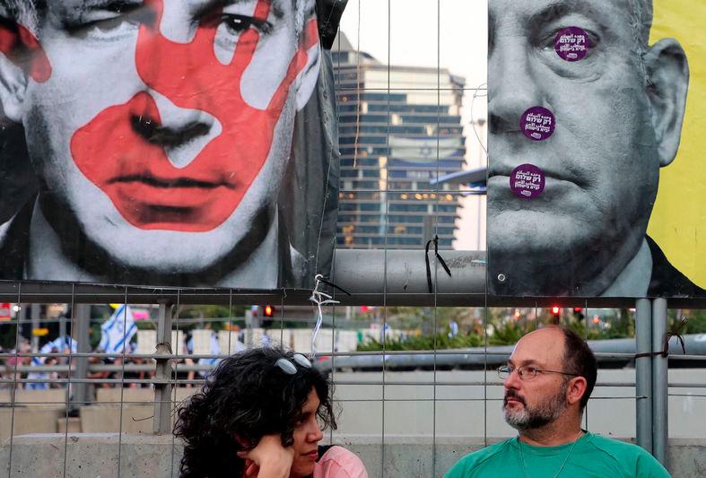 A man and woman sit under images of Israeli Benjamin Netanyahu during an anti-government rally in Tel Aviv - AFPpix
