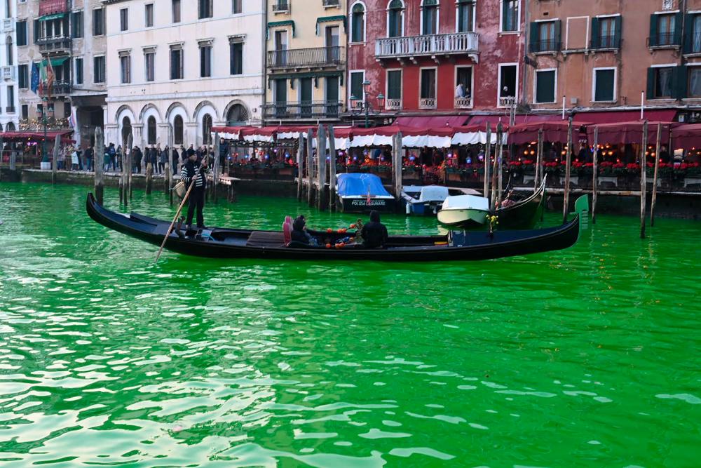 A gondola cruises on the Grand Canal after Extinction Rebellion (XR) activists poured fluorescein near the Rialto bridge in Venice to make the water fluorescent during a protest against the COP28 ‘fail’ on climate, on December 9, 2023. The banner reads “COP28 : While the Government speak we are hanging on by a thread”/AFPPix