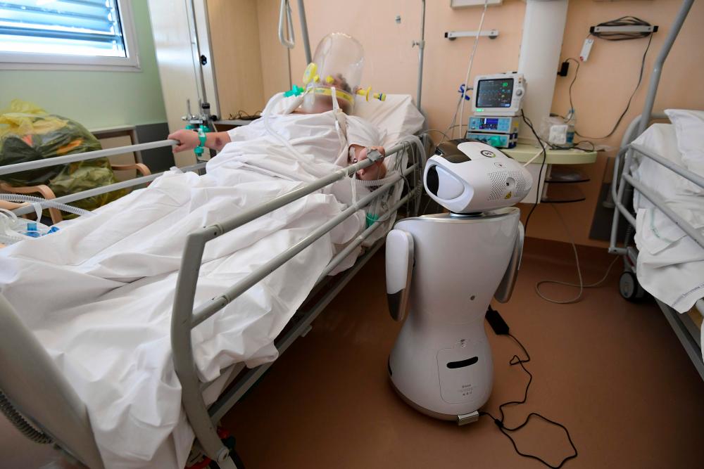 One of the six robots of the Circolo di Varese hospital stands near a patient, on April 3, 2020, to help the healthcare staff of the High Intensity Medicine department to assist twelve patients suffuring from the epedemic Covid-19, caused by the novel coronavirus. — AFP