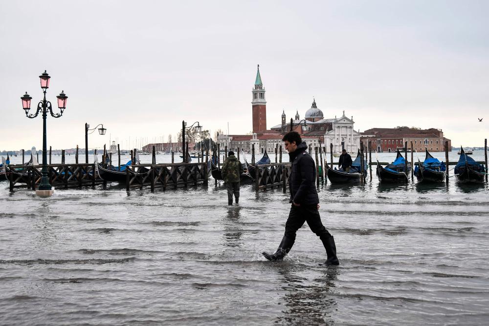 A man walks across the flooded Riva degli Schiavoni embankment with the San Giorgio Maggiore basilica in background, after an exceptional overnight Alta Acqua high tide water level, early on November 13, 2019 in Venice. - AFP