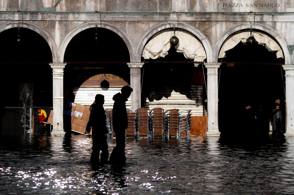 People walk across the flooded St. Mark's Square on Nov 14, in Venice. — AFP