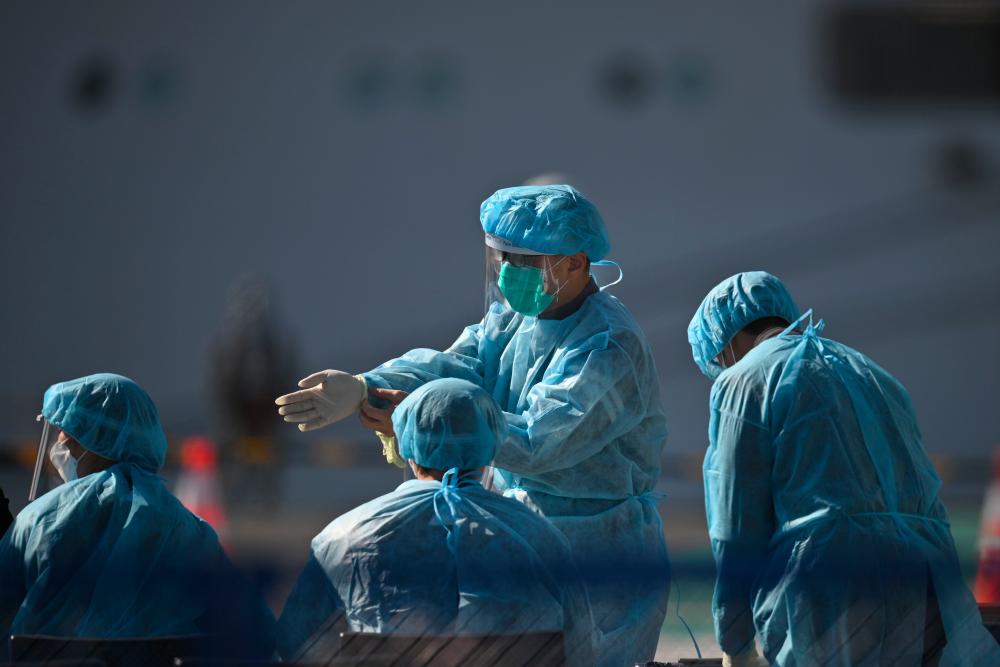 Workers in protective clothes stand before passengers disembarkating off the Diamond Princess cruise ship, in quarantine due to fears of new Covid-19 coronavirus, at Daikoku pier cruise terminal in Yokohama on Feb 21, 2020. — AFP