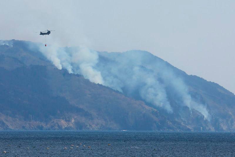 A helicopter is pictured as smoke rises due to a wildfire on a mountainside near the city of Ofunato, Iwate Prefecture - AFPpix