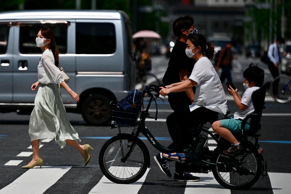 People wearing face masks amid the Covid-19 coronavirus outbreak walk across a street in Tokyo on May 13, 2020. — AFP