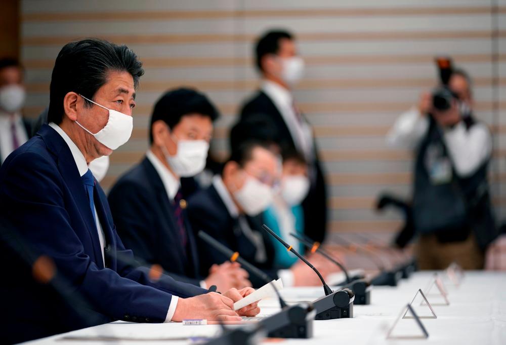 Japan's Prime Minister Shinzo Abe (L) speaks during a meeting at the headquarters for measures against the novel coronavirus disease, at the prime minister's official residence in Tokyo on April 6, 2020. - AFP
