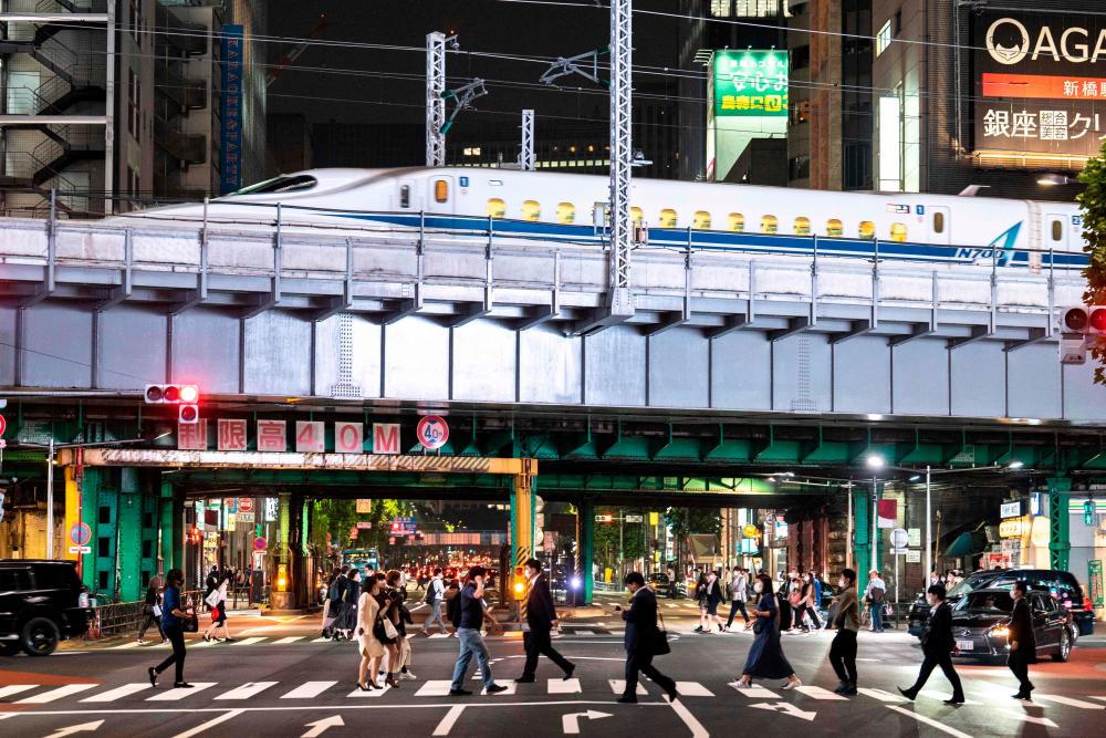 People cross a street as a shinkansen, or high speed bullet train, arrives in Tokyo on May 19, 2021. – AFP