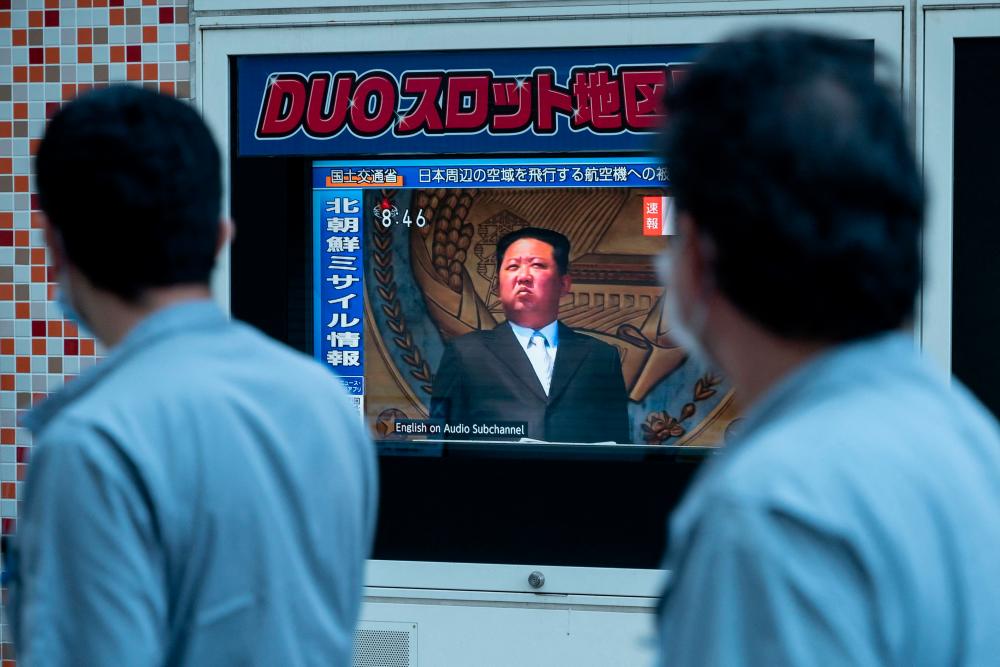 People walk past a public television screen in Tokyo on October 4, 2022, displaying file footage of North Korea's leader Kim Jong Un during a broadcast about an early morning North Korean missile launch which prompted an evacuation alert over northeastern Japan. - AFPPIX