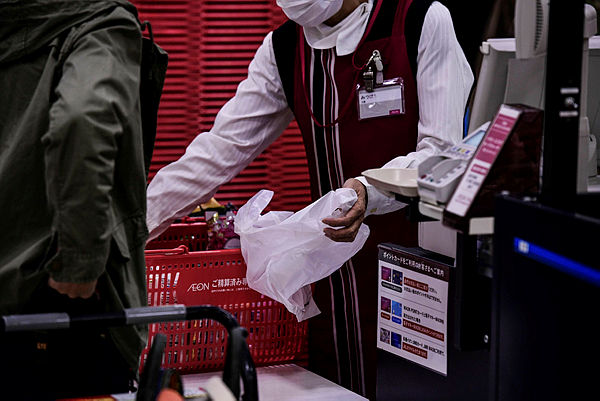 A cashier packs a customer’s products into a plastic bag in a supermarket in Chiba. — AFP