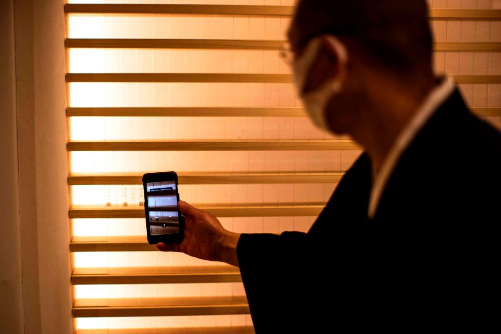 In this picture taken on February 24, 2022, Tomohiro Hirose, resident monk of Kuramae-ryoen facility, a multi-storey charnel house and Buddhist temple, scans a QR code of a departed pet dog engraved on plaques to provide some personalisation, in Tokyo/AFPPix