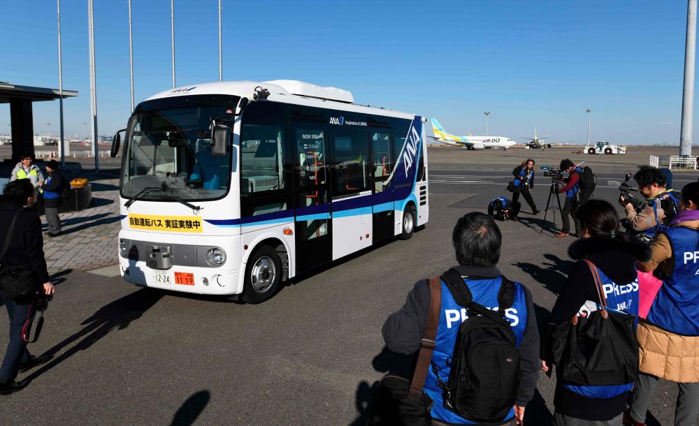 Journalists look at a driverless bus during an open test drive demonstration at Tokyo's Haneda International Airport on Jan 22, 2019. — AFP