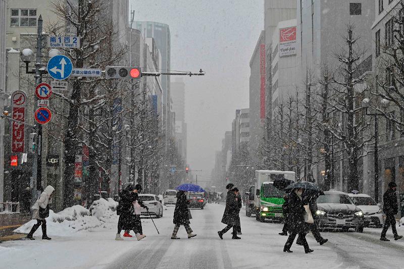 This photo taken on February 18, 2025 shows pedestrians crossing the street in the snow in central Sapporo, Hokkaido prefecture. - Richard A. Brooks / AFP