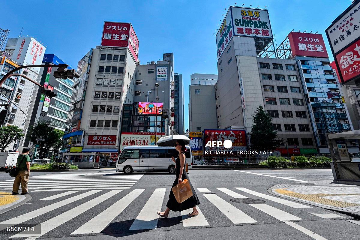 A woman (C) carries an umbrella to shelter from the sun as pedestrians cross a street in the Kabukicho entertainment area of Shinjuku in central Tokyo on July 29, 2025. - Richard A. Brooks / AFP