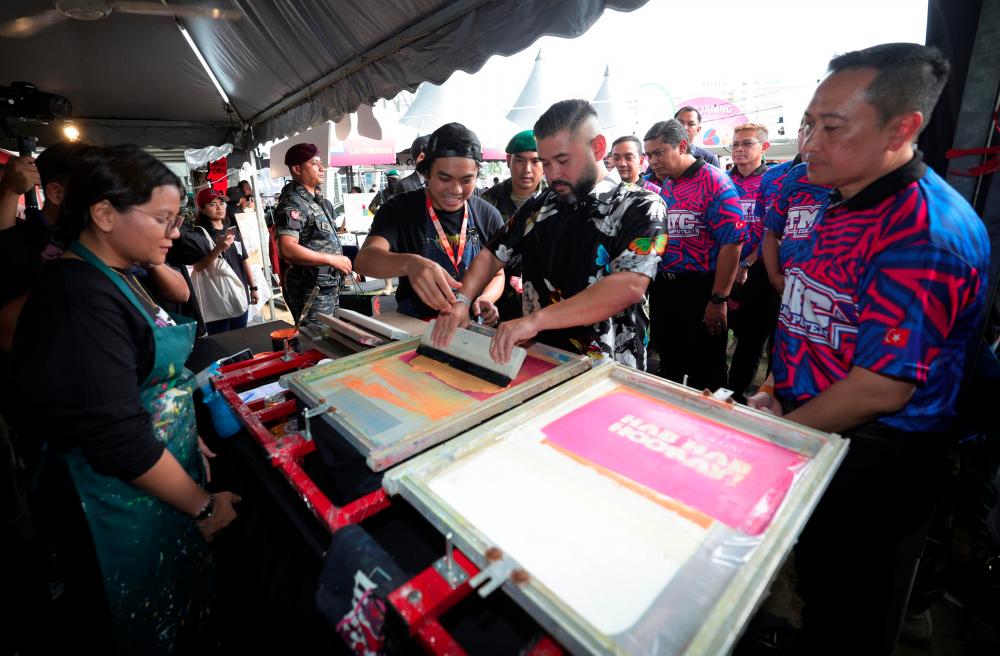 Tunku Mahkota Johor Tunku Ismail Sultan Ibrahim berkenan mencetak reka bentuk pada baju dengan dibantu pemilik Cetak Terus &amp; Co Ahmad Zaki Ariff Kassim ketika melawat pameran Hab Hab Hooray pada Majlis Pecah Tanah Tunku Mahkota Ismail Youth Center (TMIYC) Iskandar Puteri di Kompleks Sukan EduCity hari ini. - BERNAMA