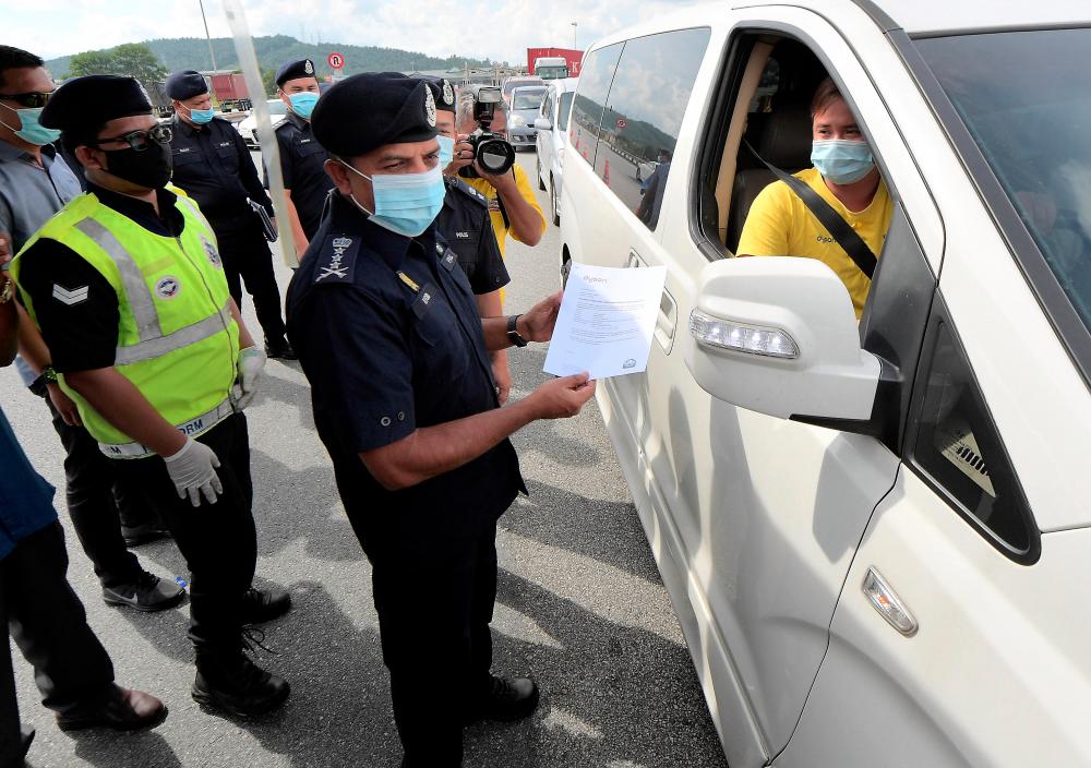 $!COMMON SIGHT ... A motorist presents a travel permit at a roadblock in Kuala Lumpur as such scenes become part of the new normal while all states except Perlis, Pahang and Kelantan observe a conditional movement control order.– ADIB RAWI YAHYA/THESUN