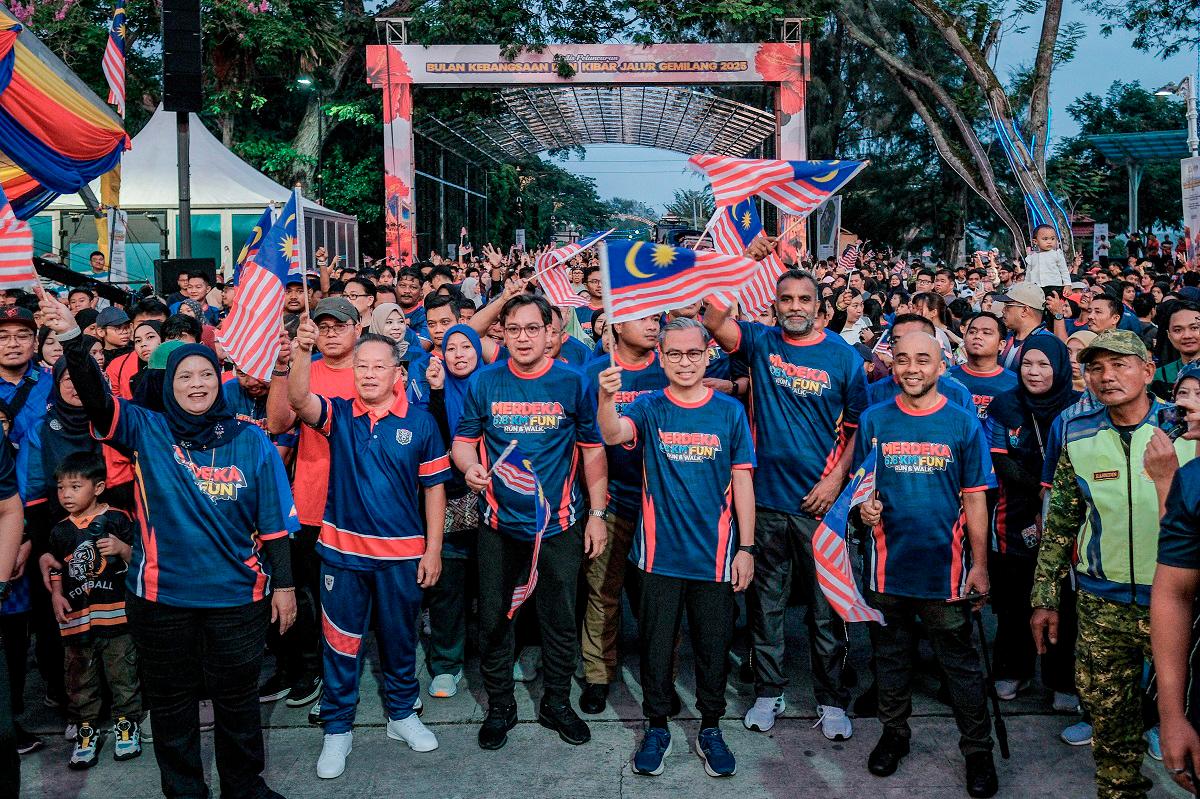 Communications Minister Datuk Fahmi Fadzil hoists the Jalur Gemilang at the Merdeka 6.8km Fun Run &amp; Walk programme in conjunction with the National Month Launch and Jalur Gemilang Flying 2025 Ceremony at Dataran Tanjung Emas, today. - Bernama pic