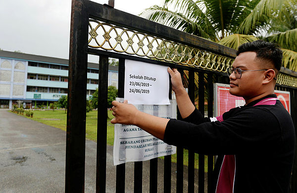 A teacher of Sekolah Agama Taman Mawar puts up a notice of the temporary closure of the school on June 22 at Johor Baru.