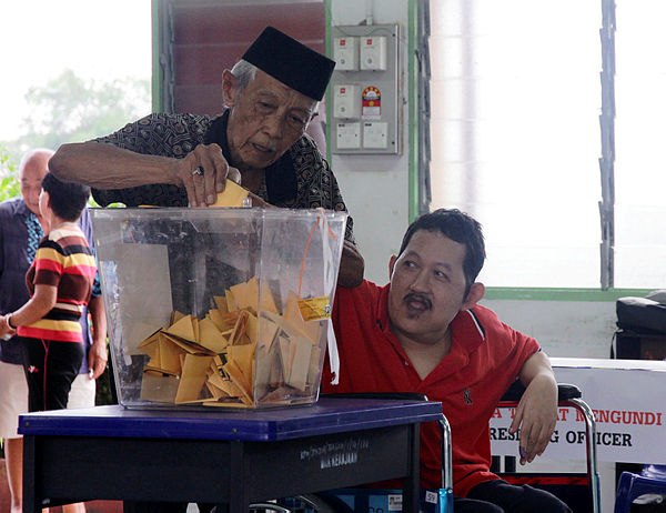 Sadiman Mortomo, 81, helps his disabled son Zulkifli Sadiman, 56, (right) to cast a vote at the Tanjung Piai by-elections today. — Bernama