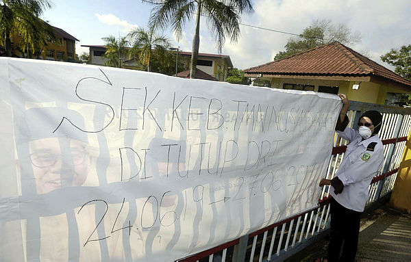 Filepix taken on June 24 shows a security guard hanging up a notice to inform of the school’s temporary closure at Sekolah Kebangsaan (SK) Taman Nusa Damai, Pasir Gudang.
