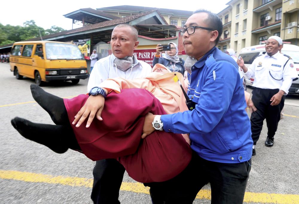 A student being assisted out of the school compound after fainting at SMK Pasir Putih, Pasir Gudang, Johor Baru on June 24, 2019. — BBX