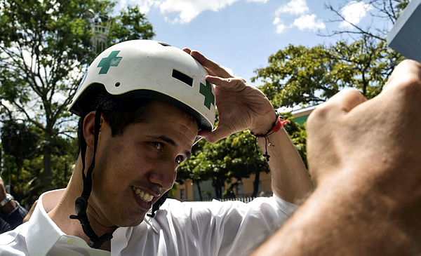 Venezuelan opposition leader and self declared acting president Juan Guaido wears a Green Cross helmet as he posses for a picture with volunteers of the movement “Aid and Freedom Venezuela Coalition” after delivering a speech in Caracas — AFP
