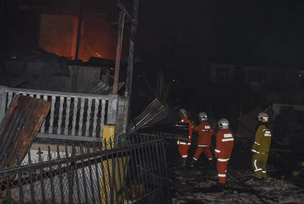 Fire and Rescue Department personnel put out the fire involving seven houses in Kampung Dusun Muda last night. - Bernama