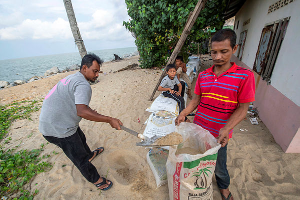 Mohammed Azmi Ramli (right) with his friend Mohammad Jefri Che, prepares wave breakers at their backyard to prevent seawater from entering their home compounds during high tides. Photo taken on 15 Nov — Bernama