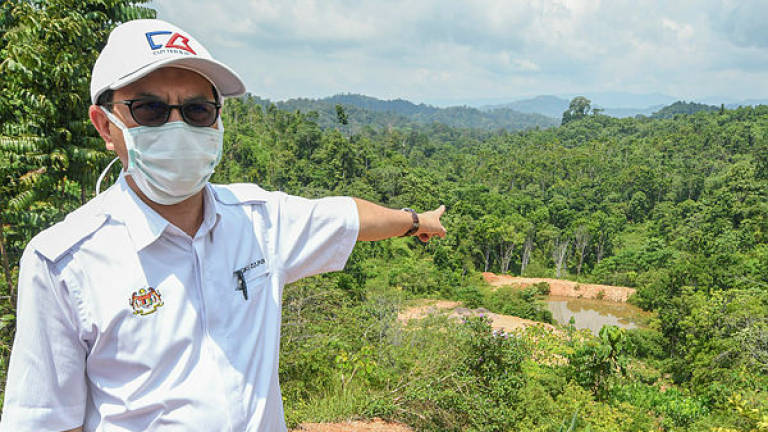 Deputy Minister of Water, Land and Natural Resources Tengku Zulpuri Shah Raja Puri points to the reservoir water from an iron ore mine near a Orang Asli settlement, while visiting the Batek Orang Asli community in Kampung Kuala Koh on June 9, 2019. — Bernama
