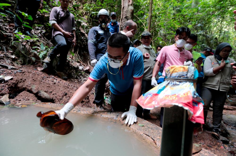 A Health Ministry staff collects a water sample from a hill water catchment area leading towards the Pertang River at Kampung Kuala Koh on June 26, 2019. — BBX