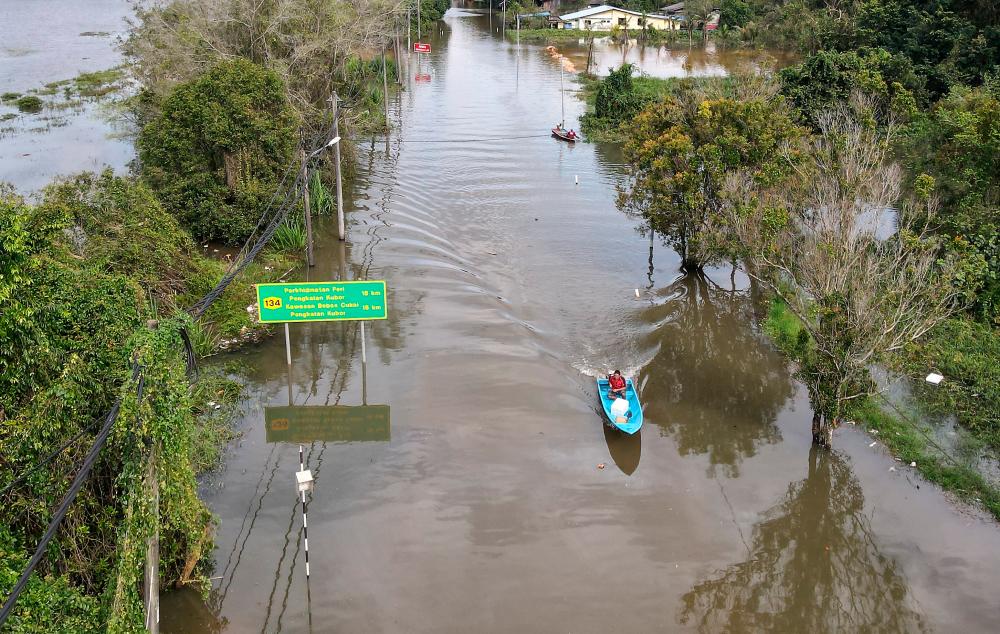 Seorang penduduk menaiki bot meredah air banjir yang melimpahi jalan di Kampung Gelang Mas ketika tinjauan fotoBernama/fotoBERNAMA