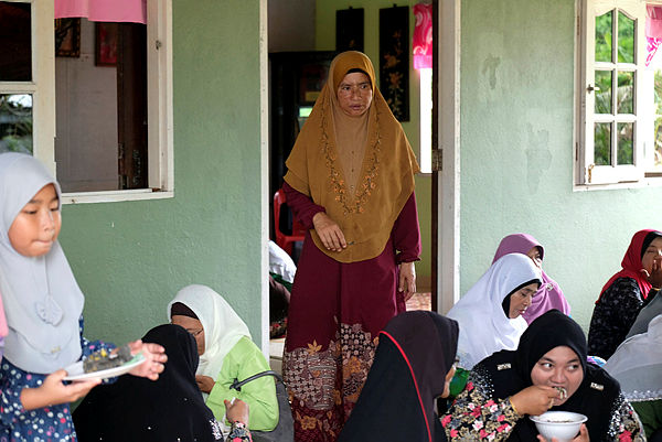 Asma Aziz (standing, centre), 52, mother of the dead fireman Muhammad Adib Mohd Kassim, during a Yassin recital at their family home in Kampung Tebengau today. — Bernama