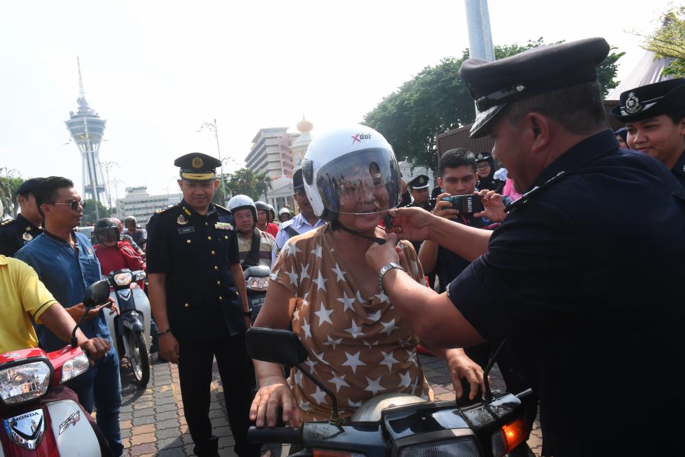 Kedah’s State Crime Prevention and Community Safety Department head SAC Dr Zainal Abidin Sabtu (R) helps a rider with her helmet at the launch of Op Selamat in conjunction with Hari Raya Aidilfitri at Dataran Medan Alor Star today. - Bernama