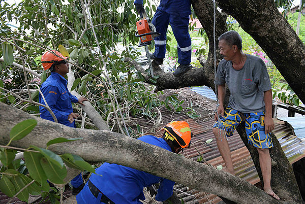 Lee Chee Phim (right), watches as personnel from the Malaysian Civil Defense Force (APM) cut a tree branch that had fallen onto his home in Alor Star, Kedah, today.