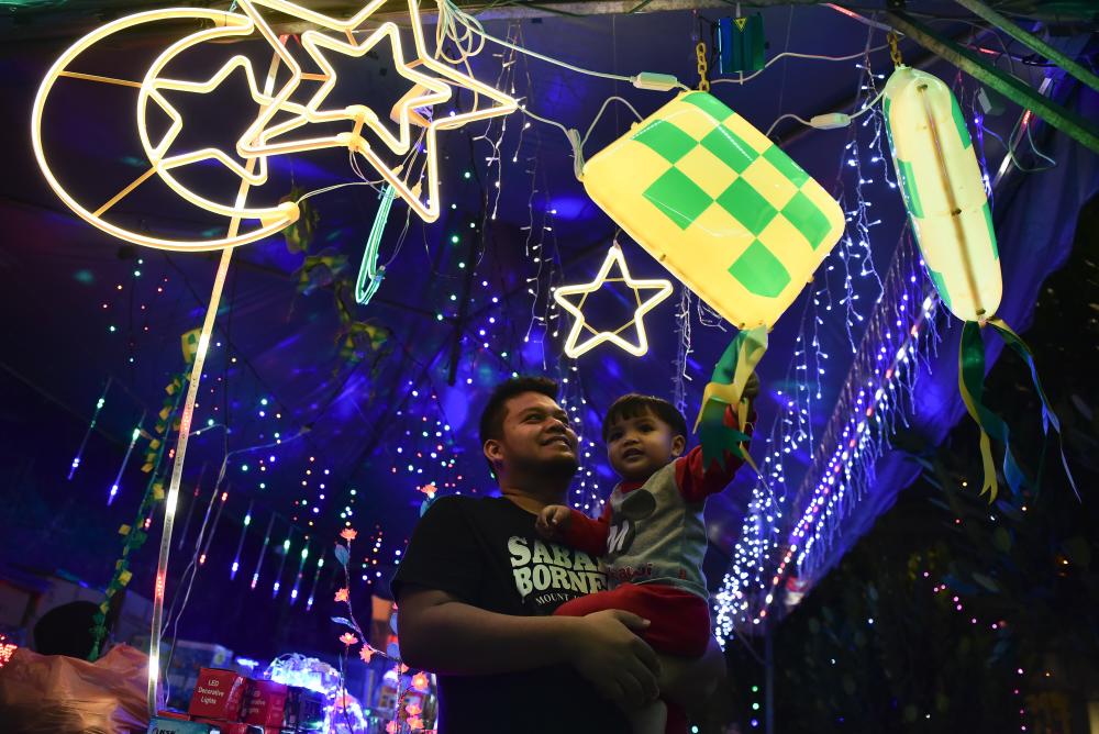 Hairul Nizam Zainul Abidin with his son Akid Anaqi enjoy the display of the ketupat, moon and stars decorated in a stall at Jalan Chow Kit at 2am this morning, the day before Hari Raya Aidilfitri. - Bernama