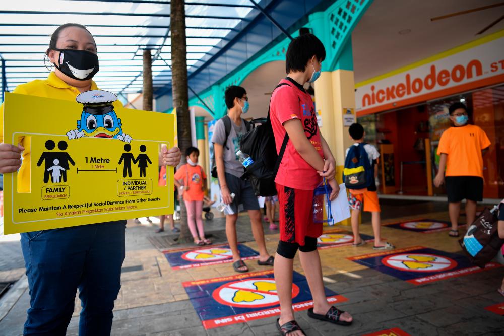 A Sunway Lagoon Theme Park staff holds a a social distancing instruction board to ensure visitors comply with SOPs during the reopening of the theme park after being closed since March 18, following the Covid-19 outbreak. - Bernama