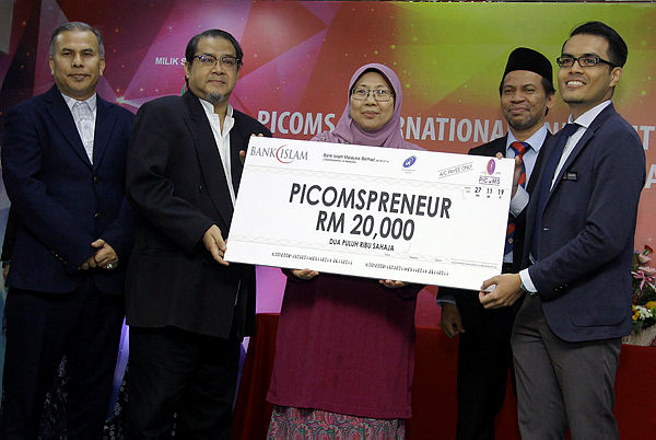 Deputy Minister in the Prime Minister’s Department (Religious) Fuziah Salleh (C) and PICOMS chairman Prof Dr Abdul Latiff Mohamed (2nd from L) hands over a replica cheque to the Dean of the Faculty of Management Azlan Abu Bakar (R) at the launch of the PICOMSpreneur programme today. - Bernama