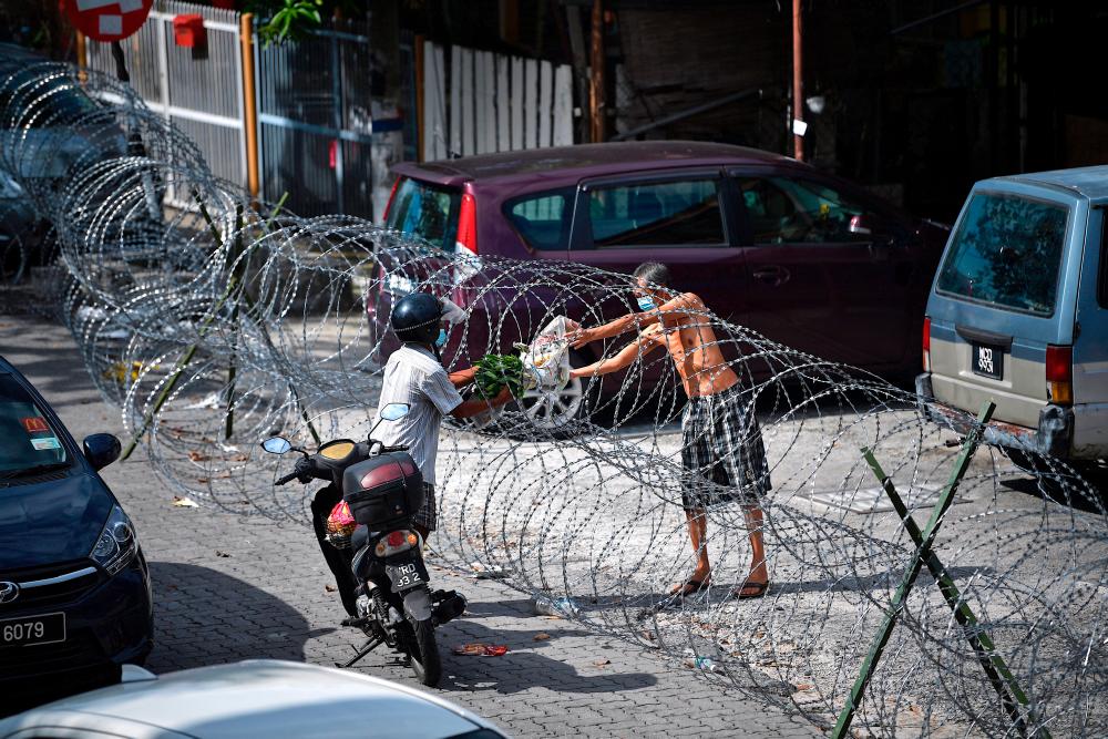 A resident of Selayang Baru collects his delivery through barbed wires, on May 4, 2020. — Bernama