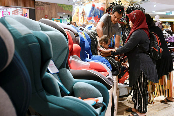 Nur Fatimah Hassan (right) tries putting her child in a Child Restraining System (CRS) at a shopping mall in Kuala Lumpur today. — Bernama