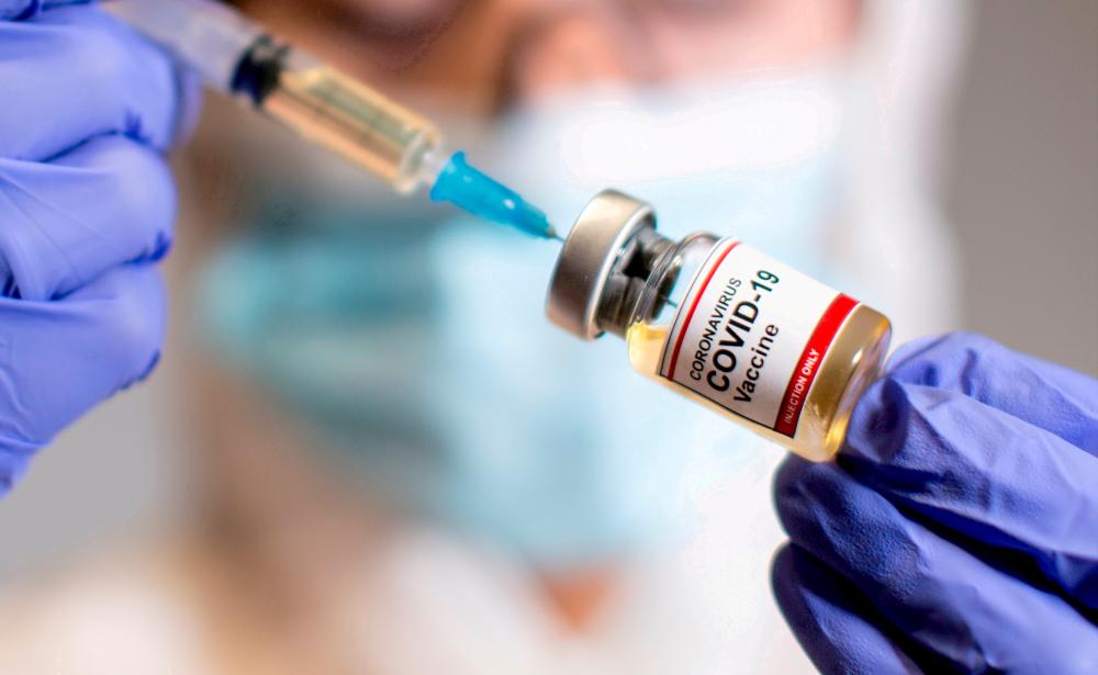 FILE PHOTO: A woman holds a small bottle labelled with a Coronavirus COVID-19 Vaccine sticker and a medical syringe in this illustration taken October 30, 2020. – Reuters