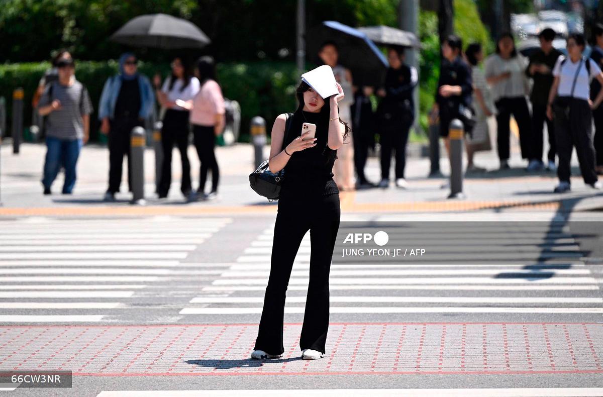A woman uses a piece of paper to shade herself from the sun as she waits to cross a road in Seoul on July 10, 2025. - Jung Yeon-je / AFP