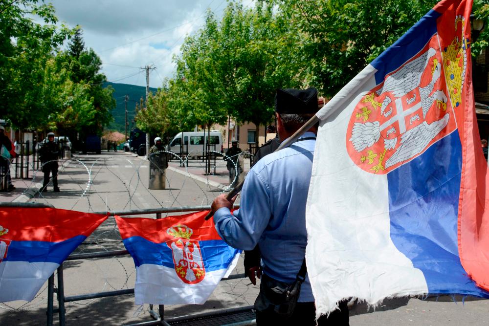 A man holding a Serbian flag looks on as he stands in front of NATO-led Kosovo Force (KFOR) soldiers in full riot gear standing behind a barbed wire perimeter around the municipal building in Zvecan. AFPPIX