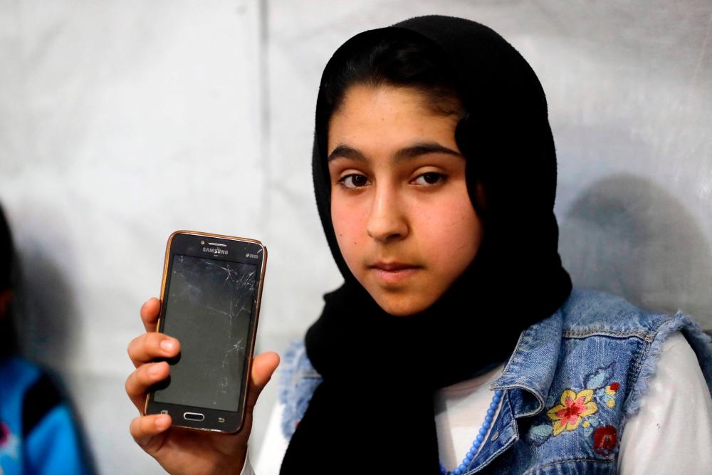 Syrian refugee Sarah, 13, shows the broken screen of her telephone, which is not suitable for online studying, at her family's tent in a refugees camp in the area of Tebrol in Lebanon's eastern Bekaa valley on April 26, 2021. – AFP
