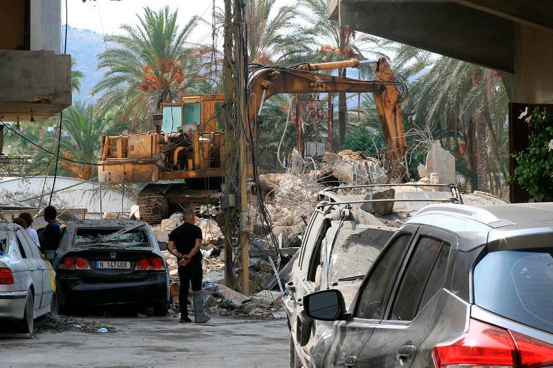 People watch as an excavator clears the rubble at the site of an Israeli airstrike in the town of Jiyeh, south of Beirut on October 6, 2024. - Mahmoud ZAYYAT / AFP