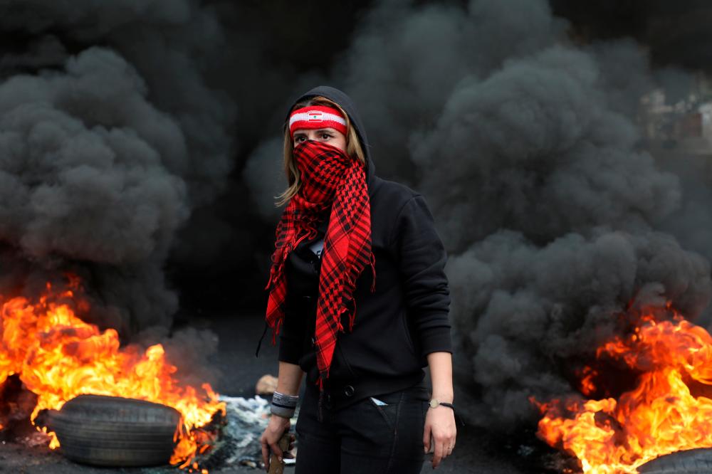 A demonstrator stands near a burning fire blocking a road, during a protest against the fall in Lebanese pound currency and mounting economic hardships, in Zouk, Lebanon March 8, 2021. — Reuters