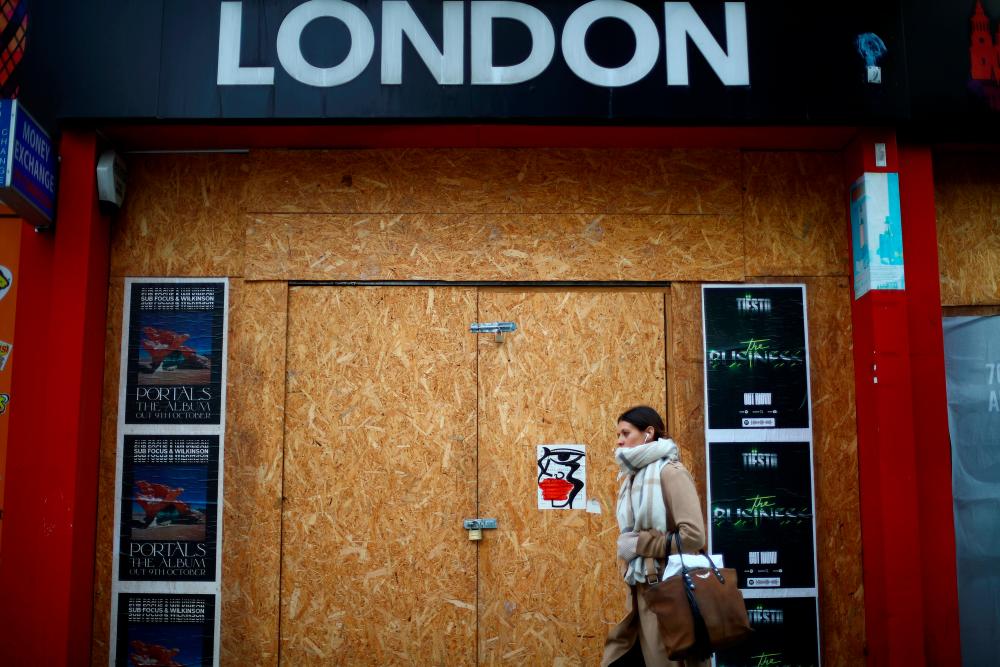 A woman walks past a boarded up London shop, amid the outbreak of the coronavirus disease (Covid-19), at Oxford Street, in London, Britain, October 14, 2020. — Reuters
