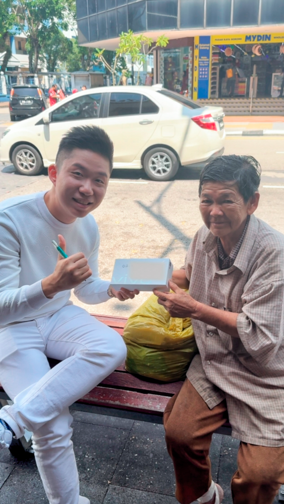 $!Luo presenting a RM600 smartphone to a senior citizen and teaching her how to use it.
