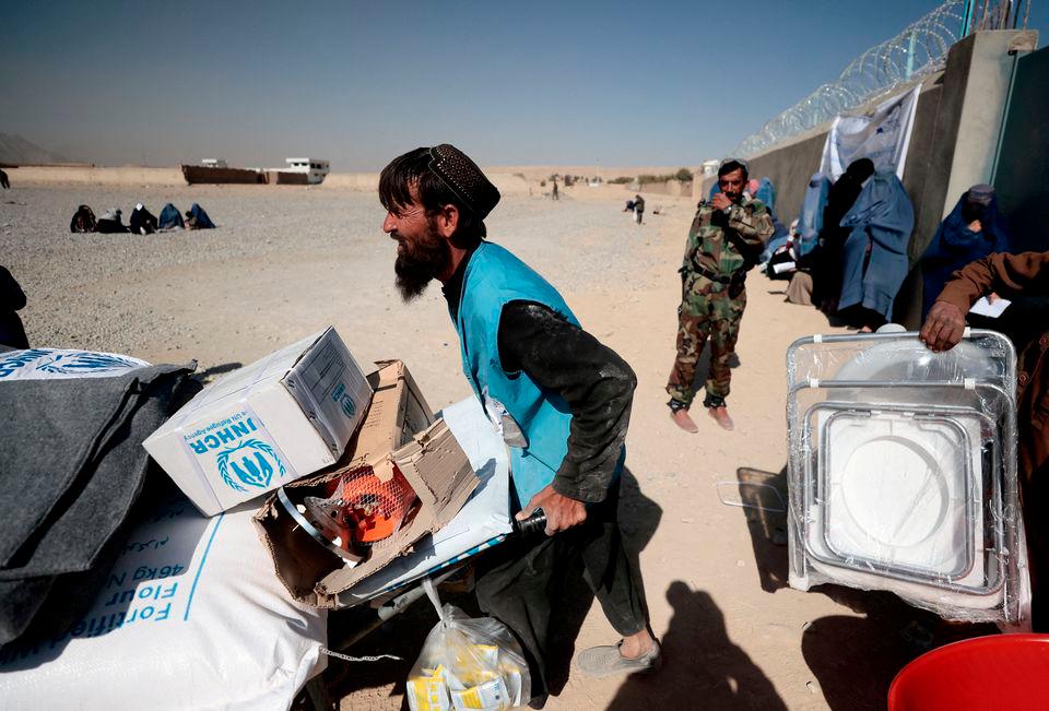 An UNHCR worker pushes a wheelbarrow loaded with aid supplies for a displaced Afghan family outside a distribution center as a Taliban fighter secures the area on the outskirts of Kabul, Afghanistan October 28, 2021. REUTERSPIX